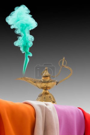 Téléchargez les photos : Ancienne lampe de génie en laiton avec fumée verte sur fond blanc et chiffons colorés - en image libre de droit
