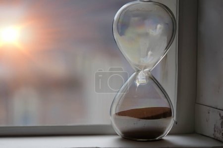Téléchargez les photos : Sablier près d'une fenêtre au lever du soleil avec de la lumière dorée - en image libre de droit