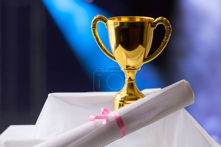 Téléchargez les photos : Trophée d'or avec certificat de réussite sur une scène avec projecteur - en image libre de droit