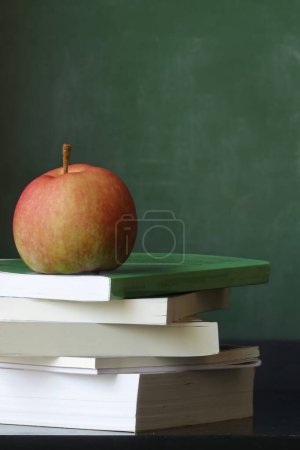 Téléchargez les photos : Pomme rouge est assis sur une pile de livres avec un tableau en arrière-plan - en image libre de droit