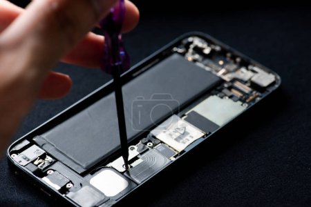 Techniker repariert Handy mit Schraubenzieher auf schwarzem Hintergrund, Nahaufnahme