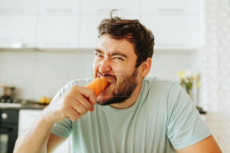 Photo for A sweet tasty carrot in the hands of a young man frustrated by the need to follow a strict diet. The guy is tired of food restrictions, he does not like vegetables. Stop diet. Front view. - Royalty Free Image