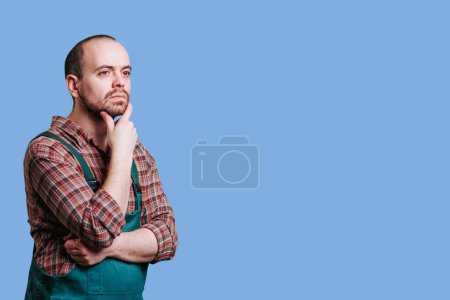 Foto de Meditative, handsome man in portrait a pensive, serious workman seems lost in thought as he gazes off into the distance. Dressed in overalls and sporting a stylish beard, copy space, thoughtful face - Imagen libre de derechos