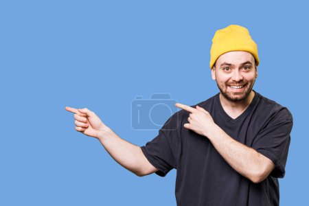 Photo for Handsome and stylish bearded guy is captured in a studio shot with copy space, pointing to free space while looking at the camera and showing expressive gestures and happy expressions. - Royalty Free Image