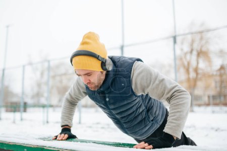 Foto de Winter Workout Warrior The image depicts a determined young adult guy training in gymnastics amidst winters chill. With headphones providing the beat, hes fully immersed in his exercise, - Imagen libre de derechos