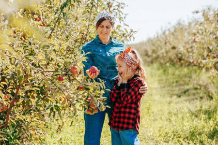 Photo for A young girl happily assisting her mother with apple picking on their farm. - Royalty Free Image