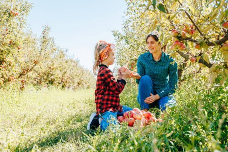Ein kleines Mädchen pflückt mit ihrer Mutter fröhlich frische Äpfel im schönen und blühenden Obstgarten der Familie.