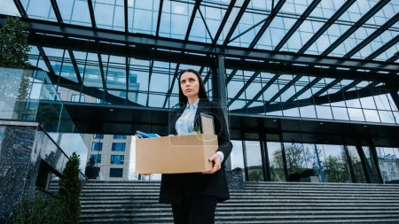Photo for Overcoming the Challenge of Work Loss and Unemployment. A white-collar employee holds a cardboard box, feeling the weight of workloss and unemployment. - Royalty Free Image