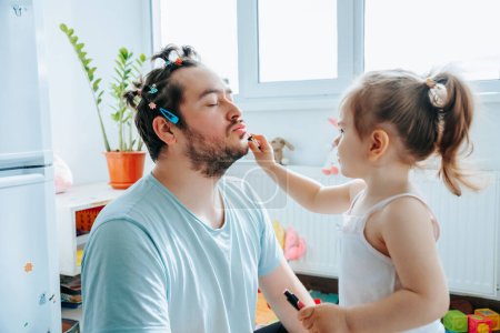Photo for Happy father and daughter spending quality time together, with the dad helping his child put on makeup and sharing a laugh. Ultimate Makeover When a Dad Decides to Try Putting Makeup on His Kid - Royalty Free Image