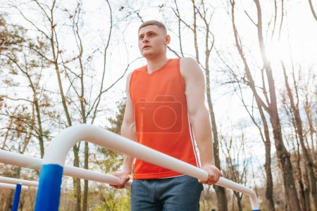 Photo for Red T-Shirt, Strong Determination A Male Athletes Outdoor Workout. The parallel bars provide the perfect platform for this male sportsman to practice his athletic skills during his outdoor training - Royalty Free Image