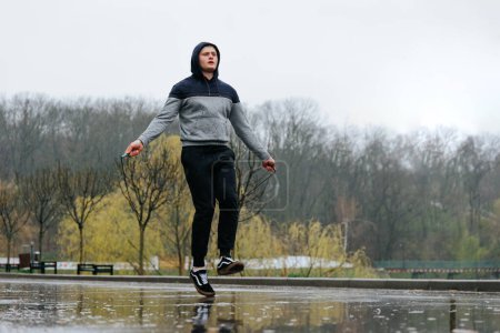 Téléchargez les photos : Corde sautante d'entraînement acrobatique sous la pluie. Un jeune athlète acrobatique brave la pluie pour s'entraîner à l'extérieur, incorporant une corde sautante pour une séance d'entraînement de haute énergie. - en image libre de droit