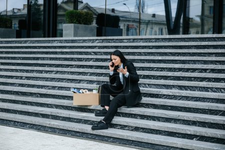 Una mujer con problemas hablando por teléfono y sosteniendo un teléfono móvil después de ser despedida de su trabajo.