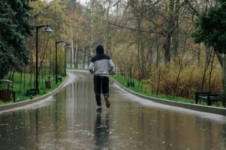 Téléchargez les photos : Man vs Rain Une bataille d'exercices en plein air. Un homme athlétique qui s'entraîne sous la pluie, son dévouement à la forme physique non découragé par la météo - en image libre de droit