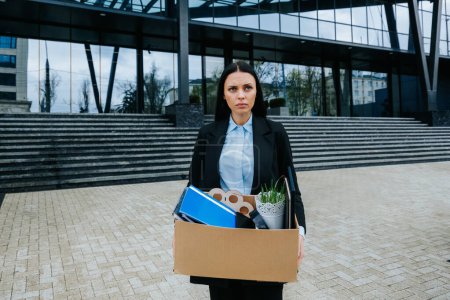 Photo for The Struggle of Finding Work After Job Loss. An upset woman holds a cardboard box, facing the uncertainty of job loss and dismissal. - Royalty Free Image