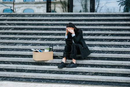Photo for The woman sitting on steps, a poignant reminder of the challenges of unemployment and the loss of work. Struggling with Job Loss A Woman Sitting on Stairs with a Cardboard Box - Royalty Free Image