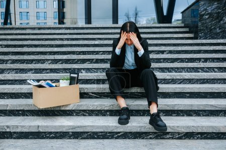 Eine düstere Szene einer Frau, die auf Stufen sitzt und mit dem Verlust ihrer Arbeit und der Schwierigkeit, arbeitslos zu sein, umgeht. Unzufriedene Brünette sitzt nach Jobverlust auf Treppe