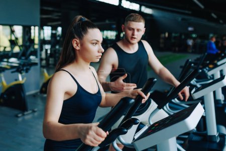 Téléchargez les photos : Un entraîneur de fitness dédié instruisant un jeune homme et une femme lors d'une séance d'entraînement dynamique dans une salle de gym bien équipée, favorisant un mode de vie sain et actif. - en image libre de droit