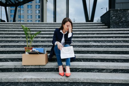 features a woman in her middle age, visibly worried and upset, sitting on a stair amidst an outdoor setting, capturing the profound impact of job loss, unemployment,
