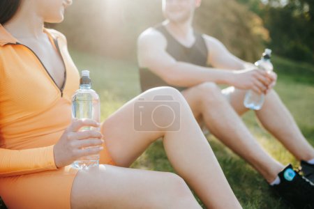 Photo for Two young adults, both athletes, a man, and a woman, in sportswear, engaging in conversation and enjoying the outdoors after their workout. The man holds a water bottle, - Royalty Free Image