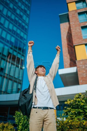 Photo for Vertical shot An Asian Korean student boy celebrates his victory outdoors with a radiant smile that reflects happiness, satisfaction, and youthful exuberance, - Royalty Free Image