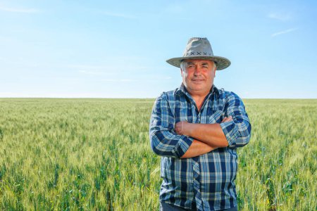 Älterer Bauer auf einem landwirtschaftlichen Feld blickt in die Kamera, während er auf einem Feld mit grünen Pflanzen in der Landschaft steht