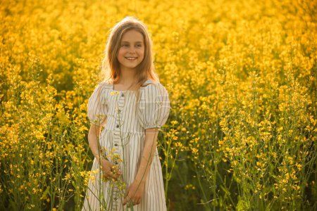 Téléchargez les photos : Portrait artistique d'une jolie petite fille rieuse dans la robe, la prairie au printemps avec du colza fleuri. rustique, beaux-arts - en image libre de droit