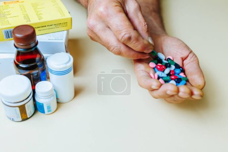 Studio Schuss Nahaufnahme Handvoll Pillen in der Hand unkenntlich andere Hand nimmt eine der Tabletten aus der Handfläche. Im Hintergrund Plastikdosen mit Tabletten.