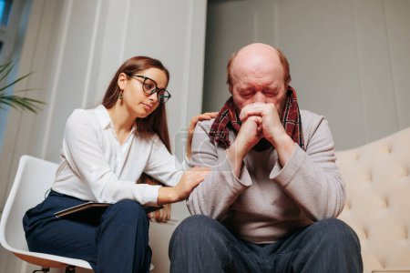 Elderly man sits hands to face, he has grief, young psychologist woman holds her hands on shoulder of man. Specialist support, psychotherapist, assistance. sadness, depression, feeling of loneliness.