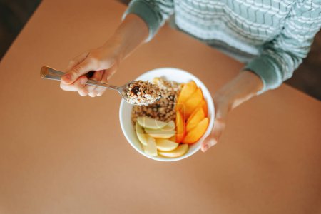 Top view spoon with granola in unrecognizable female hand close up. Plate of raw fruit in a woman hand. Advertising healthy breakfast for weight loss. Healthy food concept.