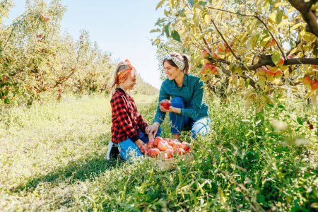 Une mère fière et sa fille exhibant les délicieuses pommes qu'ils cueillaient ensemble dans leur verger luxuriant.