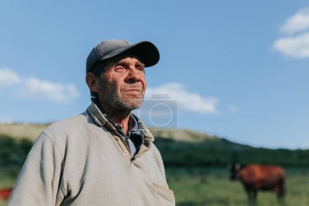 Vor dem Hintergrund der ländlichen Landschaft zeigt dieses Porträt einen älteren Bauern mit Hut und verwitterten Gesichtszügen, die Bände über sein Leben und seine Arbeit im Freien sprechen..