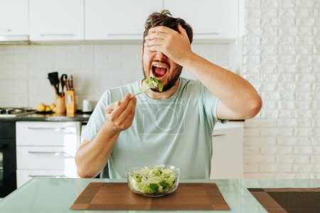 A young man brings a fork to his open mouth to eat salad with his eyes closed. The main thing is to be healthy, so you need to eat healthy food. Diet food concept. Stop diet.
