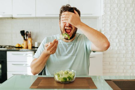 Front view covering his face with his hand, in the other hand a fork with a salad brought to his open mouth. Diet fatigue. The concept of a healthy lifestyle. Stop diet.