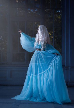 Foto de Hermosa mujer con un elegante peinado rizado. Princesa. Un lujoso vestido azul con un tren largo - Imagen libre de derechos