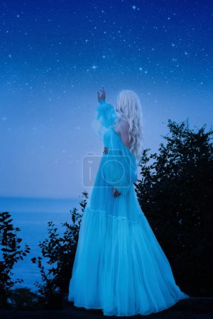 Foto de Un lujoso vestido azul con un tren largo revolotea en el viento. Foto de atrás sin rostro. La mujer busca las estrellas - Imagen libre de derechos