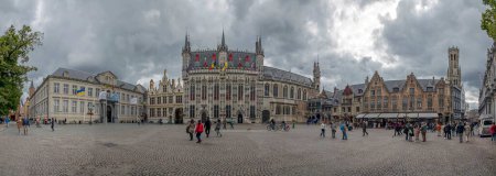 Photo for Bruges, Belgium - September 18, 2022: Large panorama of Burg Square with Bruges City Hall in center under the dramatic cloudy autumn sky. Tourists, beautiful vintage buildings and flags - Royalty Free Image