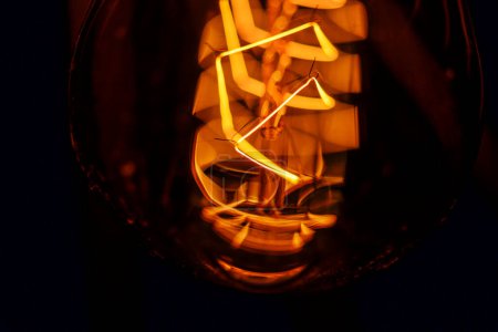 Photo for Close-up of bright yellow spiral of a filament lamp. Vintage light bulbs in darkness, abstract background - Royalty Free Image
