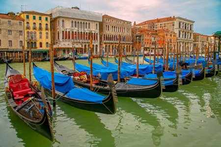 Venice, Italy - February 27, 2023: Gondola station Traghetto di Riva del Vin on the Grand Canal, with row of the moored gondolas at sunset. Medieval architecture in the background, perspective view