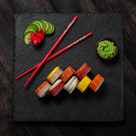 Téléchargez les photos : Vue sur la cuisine japonaise au restaurant. Sushi de saumon sur plaque mate en pierre noire sur fond de table en bois rustique. Ensemble avec baguettes rouges, gingembre et wasabi vert. Espace de copie, pose plate - en image libre de droit