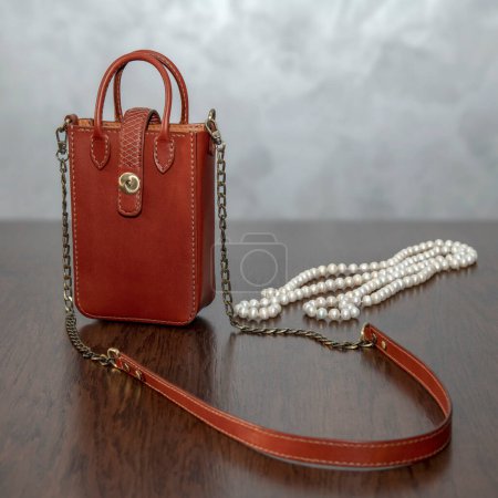 Téléchargez les photos : Élégant sac femme en cuir marron élégant et collier de perles sur une table en bois. Sac à main féminin à la mode - en image libre de droit