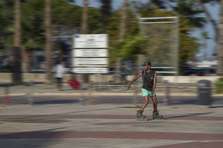Téléchargez les photos : Larnaca, Chypre - 01 avril 2024 : Un homme énergique sur patins à roulettes se déplace le long du trottoir et écoute de la musique. Sport, santé, vitesse, flou du mouvement et énergie - en image libre de droit