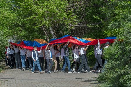 Téléchargez les photos : Erevan, Arménie - 23 avril 2024 : Marche des élèves arméniens avec un énorme drapeau arménien au Tsitsernakaberd à l'occasion de l'anniversaire du génocide arménien de 1915. Contraste du drapeau coloré contre la forêt verte - en image libre de droit