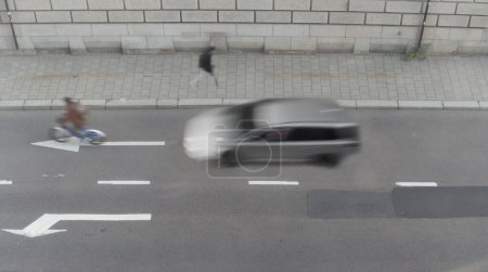 Photo for High angle view of street with arrows on asphalt, cyclist, pedestrian and a car in blurred motion - Royalty Free Image