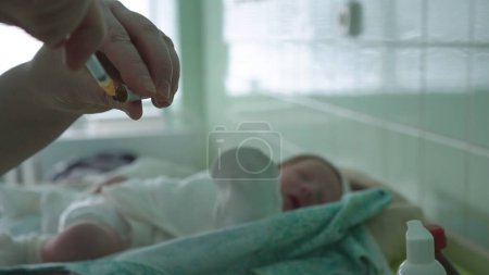 Foto de Un médico sin guantes introduce una vacuna en una jeringa para inyección a un recién nacido. En el fondo, un bebé recién nacido está fuera de foco. Vacunación en el hospital. Violación de las normas sanitarias - Imagen libre de derechos