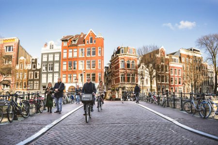 Foto de Ámsterdam, Países Bajos - 13 de marzo de 2023: Personas montando bicicletas y caminando por el canal de agua en la ciudad vieja de Ámsterdam - Imagen libre de derechos