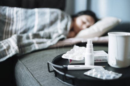 Photo for A girl suffering from a seasonal cold lies in bed. Antiviral drugs on a tray - Royalty Free Image