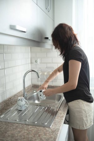 Téléchargez les photos : Une jeune fille qui lave la vaisselle. L'adolescent aide à la routine à la maison - en image libre de droit