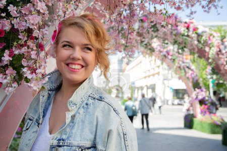Téléchargez les photos : Portrait d'une grosse fille en vacances au printemps dans une belle rue en plein air entourée de fleurs. - en image libre de droit