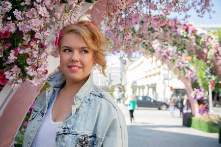 Téléchargez les photos : Portrait d'une fille dodue en vacances au printemps dans une belle rue en plein air entourée de fleurs. - en image libre de droit