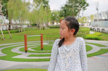 Photo for Angry Asian young girl kid turn her face to the side and eyes closed while sitting in the garden outdoor. - Royalty Free Image
